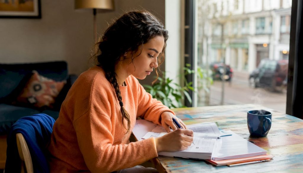 Een vrouw zit aan de keukentafel verdiept in haar taalcursus.