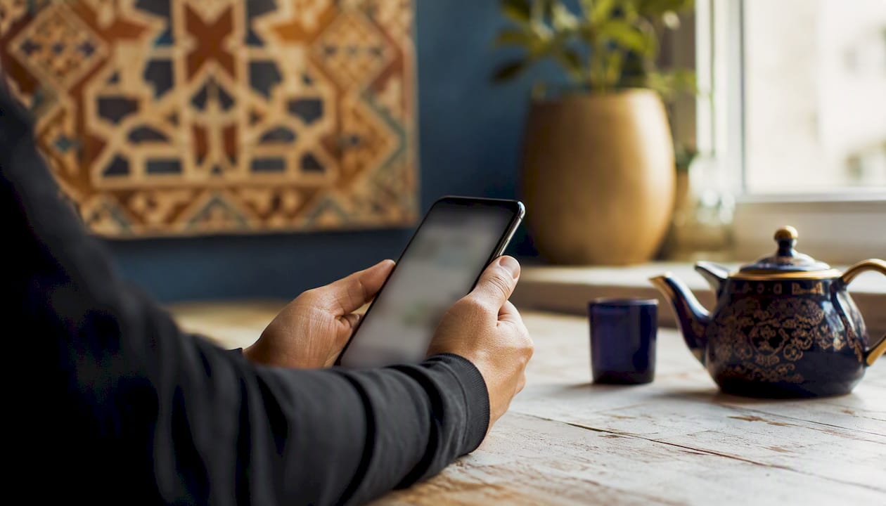 Een paar handen houdt een smartphone vast, omringd door materialen om Arabisch te leren.