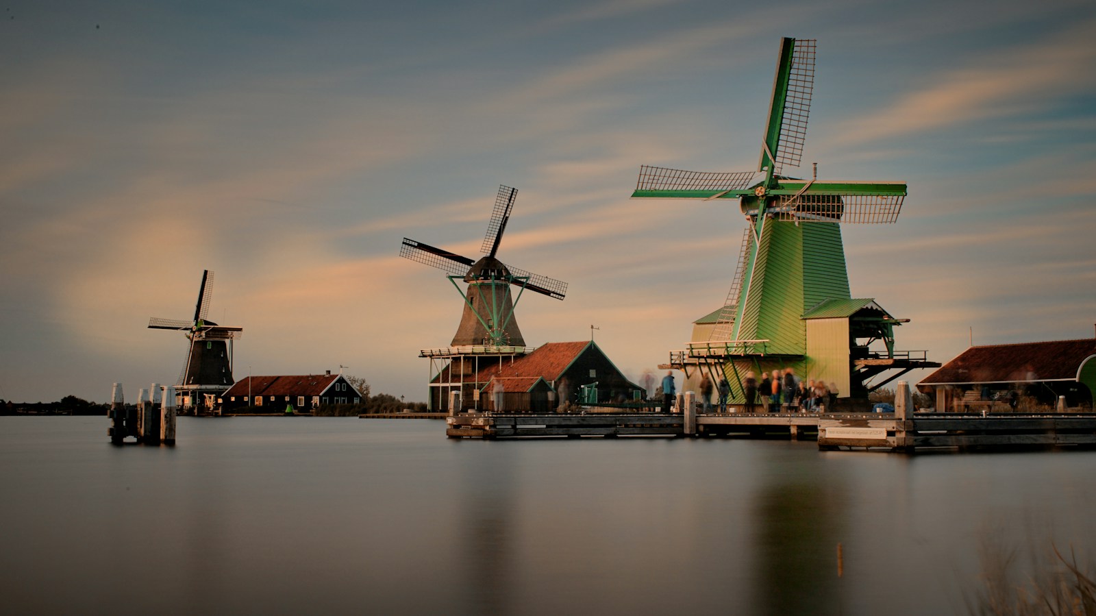 Drie volledig zichtbare molens aan het water bij de Zaanse Schans in avondlicht